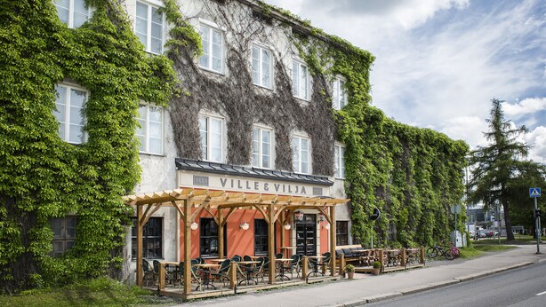 A building with ivy-covered walls and a covered outdoor seating area with tables and chairs. - Hotelli Ville (Tampere)