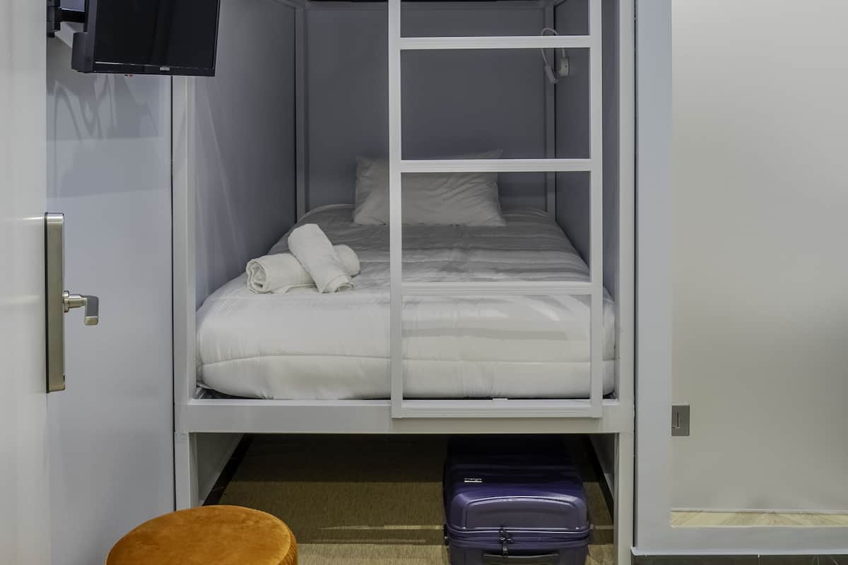 A bunk bed room with a television mounted on the wall, a suitcase under the lower bunk, and a door to the right.