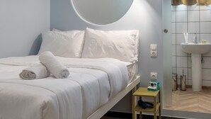 A modern hotel room with a neatly made bed, a small bedside table with a lamp, a suitcase, and a mirror above the sink. - Cabins Sleeping Mets (Athens)