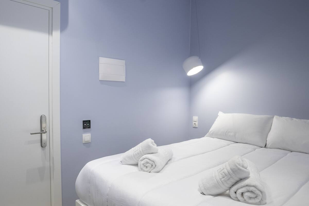 A hotel room with a bed, white towels, a door, and a light fixture.