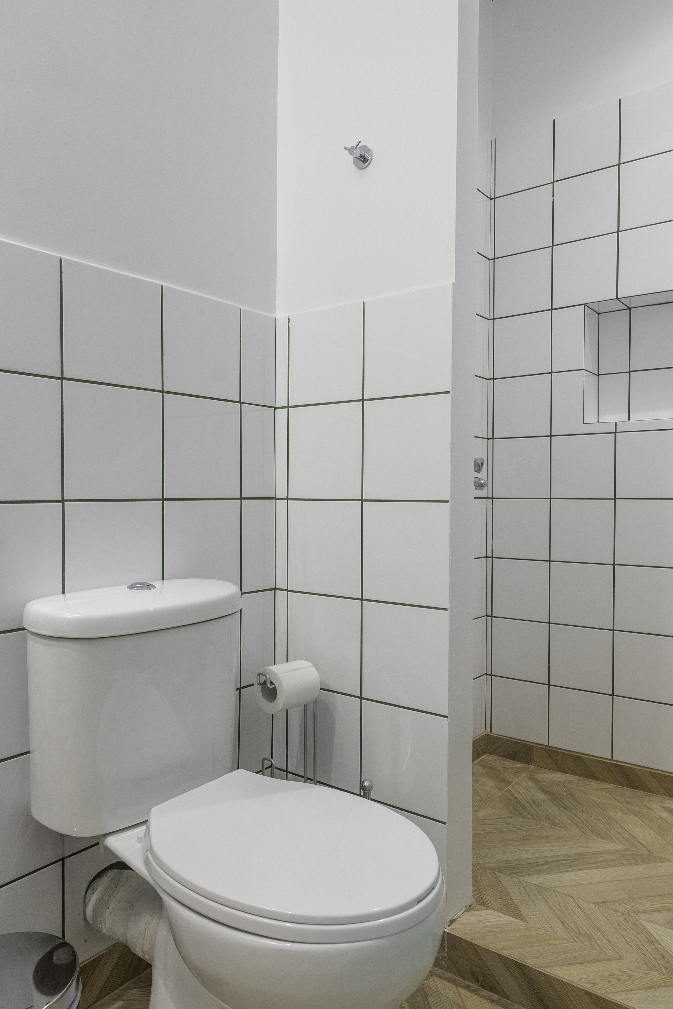 A modern bathroom with a white toilet, a wooden floor, and a tiled wall with a grid pattern.