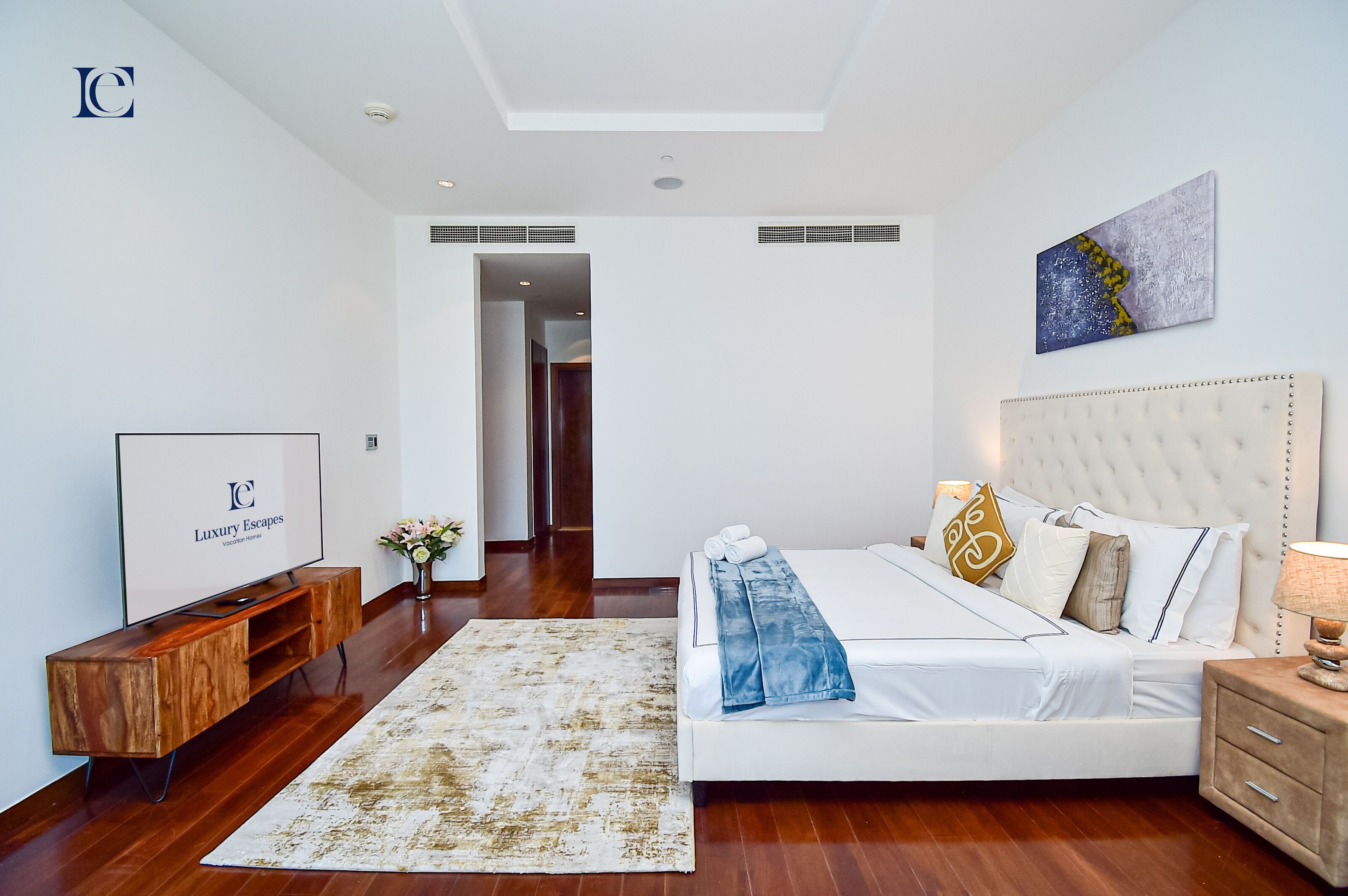 A modern bedroom with a large bed, a TV, and a wooden console.