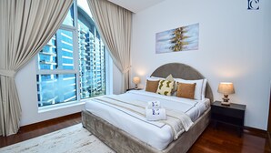 A modern hotel room with a large bed, a view of a cityscape through a large window, and a painting on the wall. - Premium 3BR Partial Sea View OCEANA (Dubai)