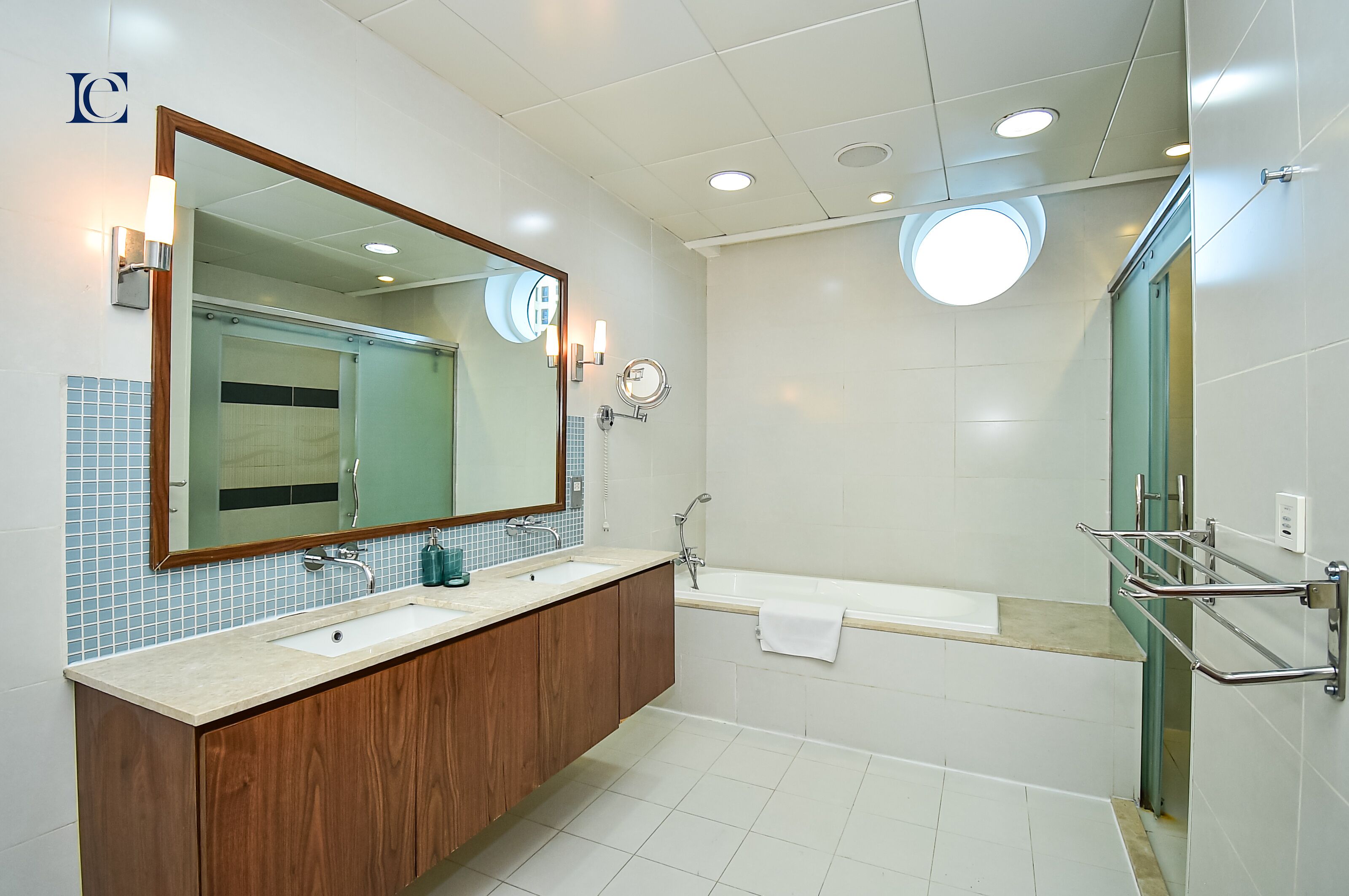 A modern bathroom with a large mirror, two sinks, a bathtub, and a glass shower enclosure.