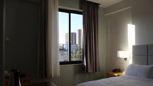 A hotel room with a large bed, a nightstand, a lamp, and a window with curtains. - Cot Hotel (Addis Ababa)
