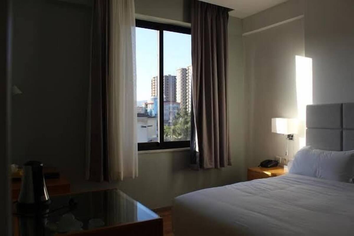 A hotel room with a large bed, a nightstand, a lamp, and a window with curtains.