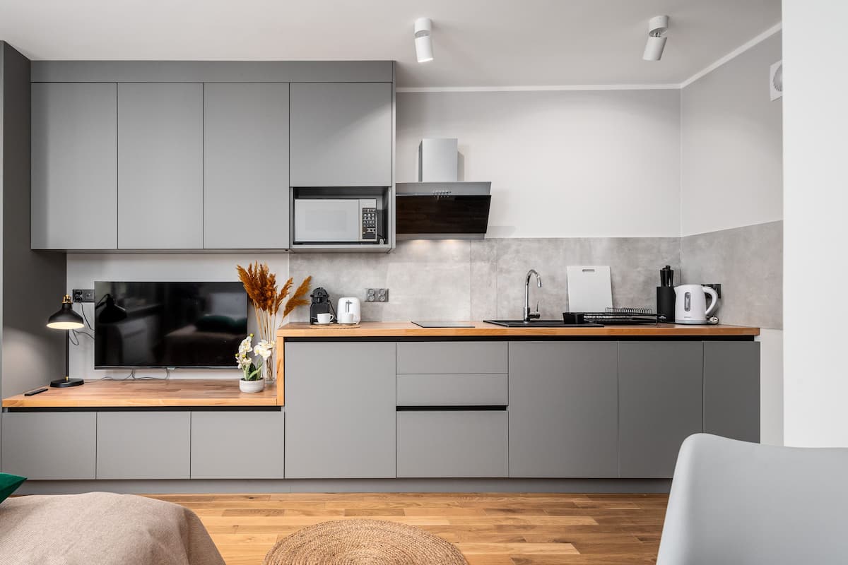 A modern kitchen with grey cabinets, a flat-screen TV, a microwave, and a coffee maker.