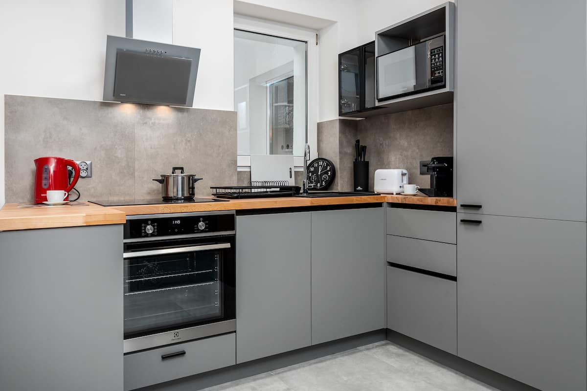 A modern kitchen with grey cabinetry, a built-in oven, a microwave, and a red kettle.