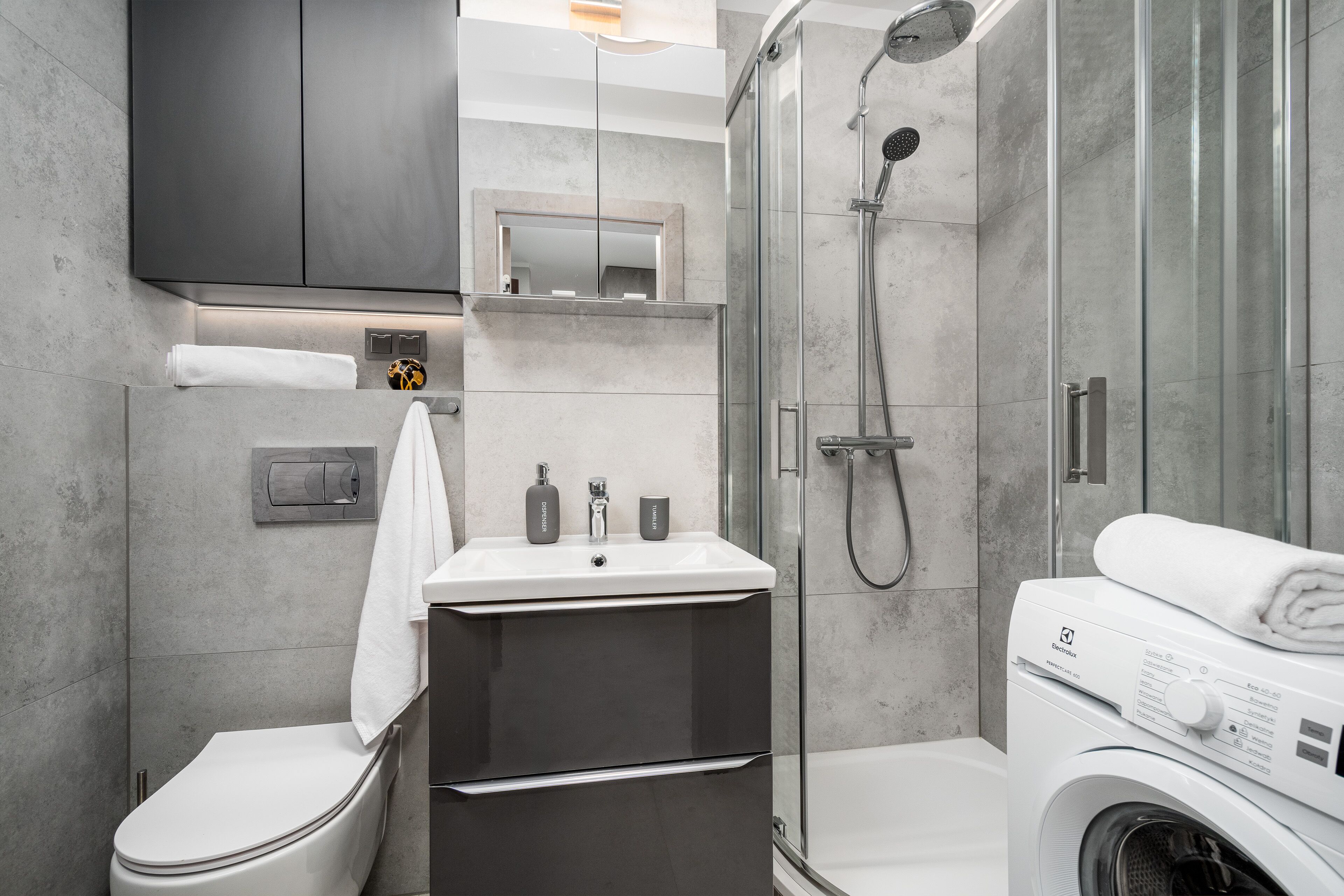 A modern bathroom with a toilet, sink, shower, and washing machine.