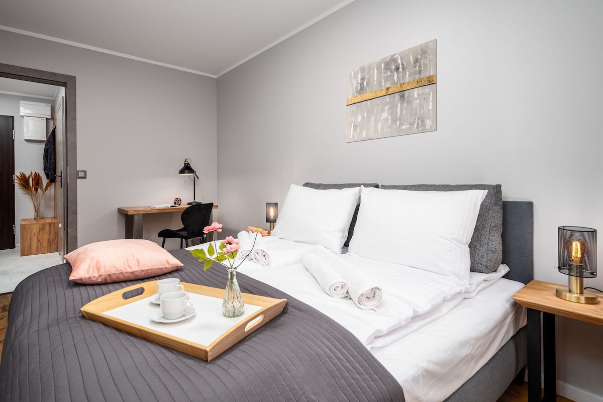 A modern hotel room with a bed, bedside tables, a desk, and a chair.