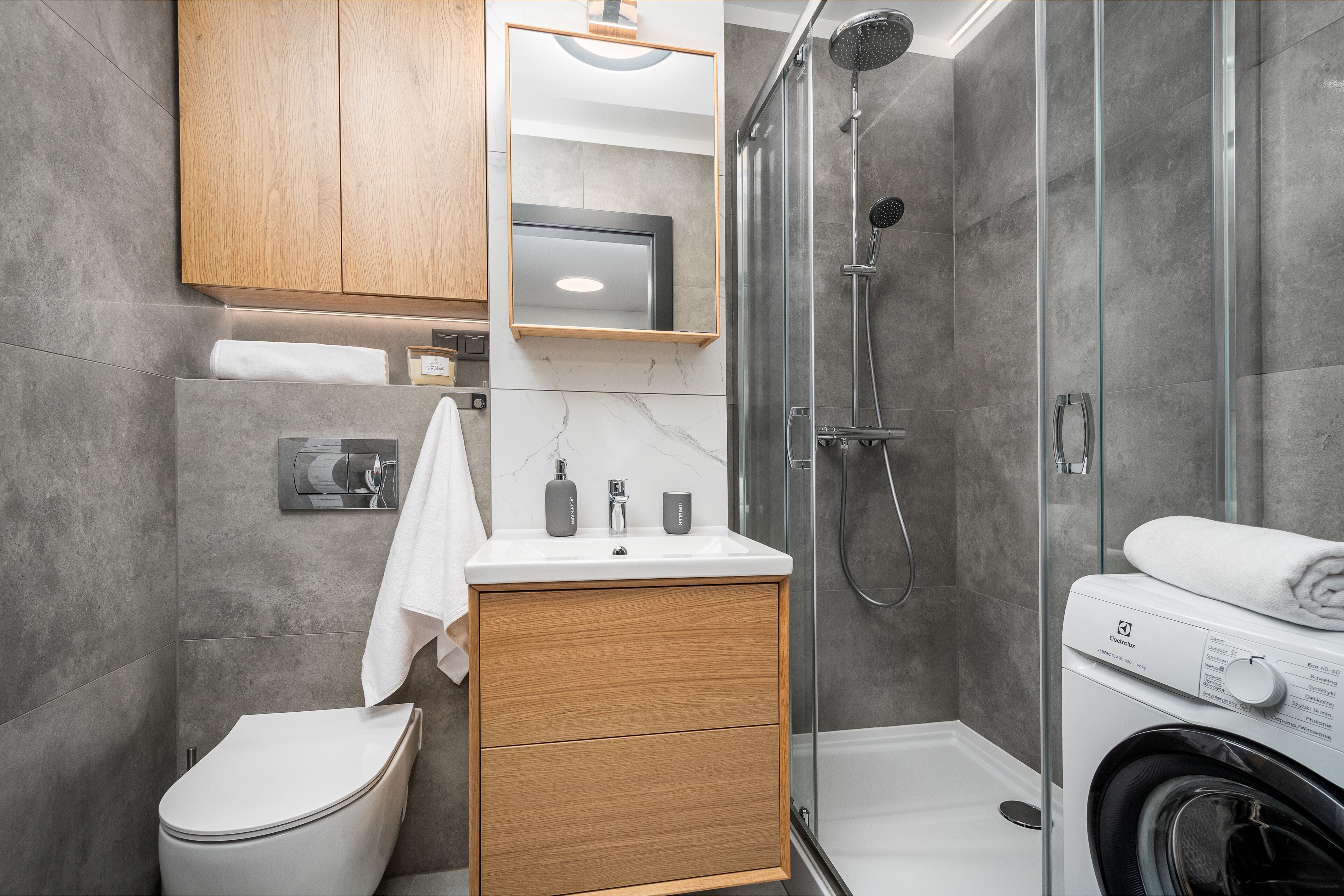 Une salle de bain moderne comprenant des toilettes, un meuble en bois, un miroir, un lavabo et une douche à parois de verre.