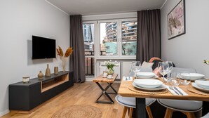Ein moderner Essbereich mit einem Holztisch, gedeckt für vier Personen, einer schwarzen Unterhaltungsanlage und einem großen Fenster mit Vorhängen.