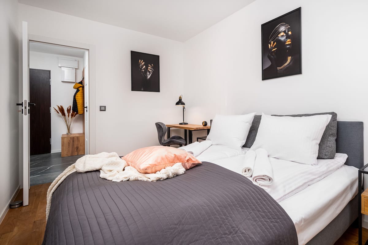 A modern bedroom with a bed, bedside table, lamp, and artwork on the walls.