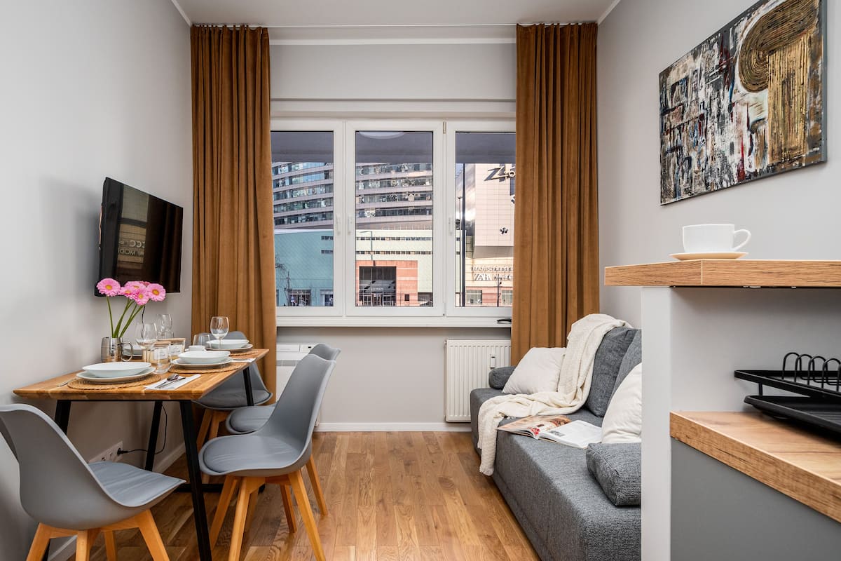 A compact living space with a dining area, a sofa, a TV, and a window with curtains.