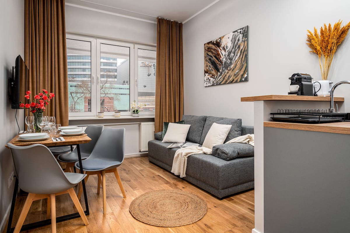 A modern living space with a dining area, a grey sofa, a kitchen island, and a window with curtains.