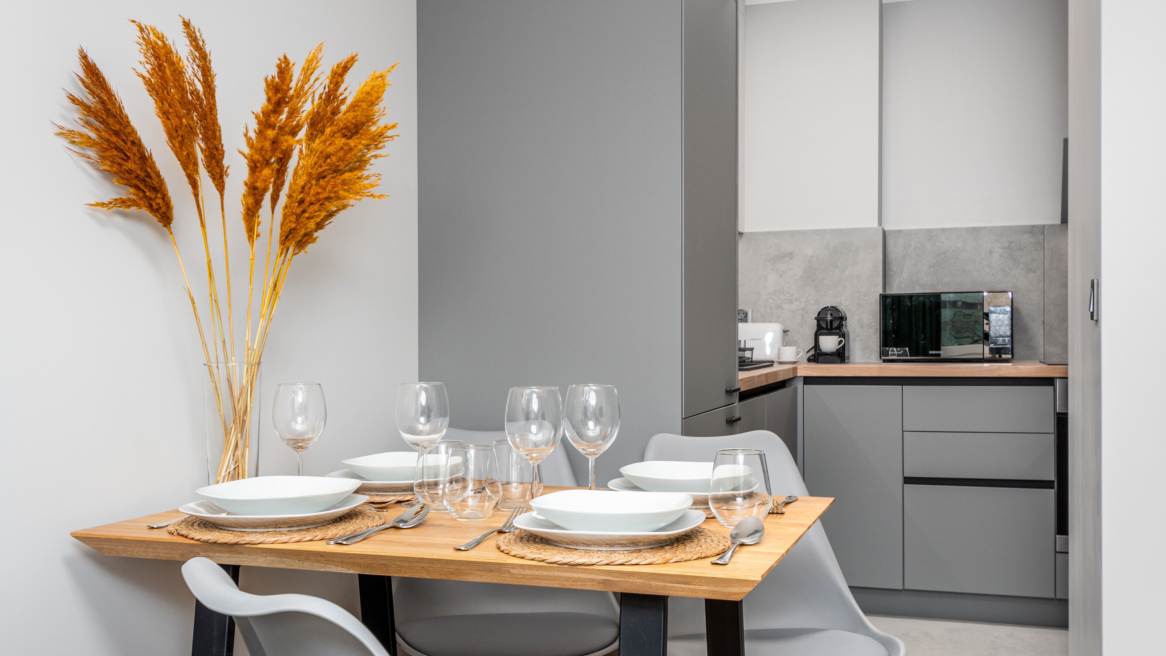 A modern dining area with a wooden table set for four, surrounded by white chairs.