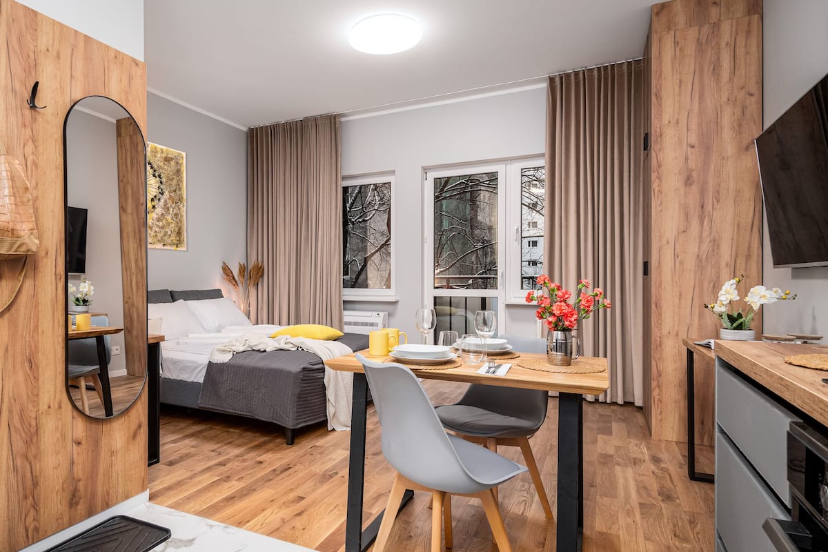 A compact hotel room with a bed, bedside table, mirror, and a small dining area with a table and chairs.