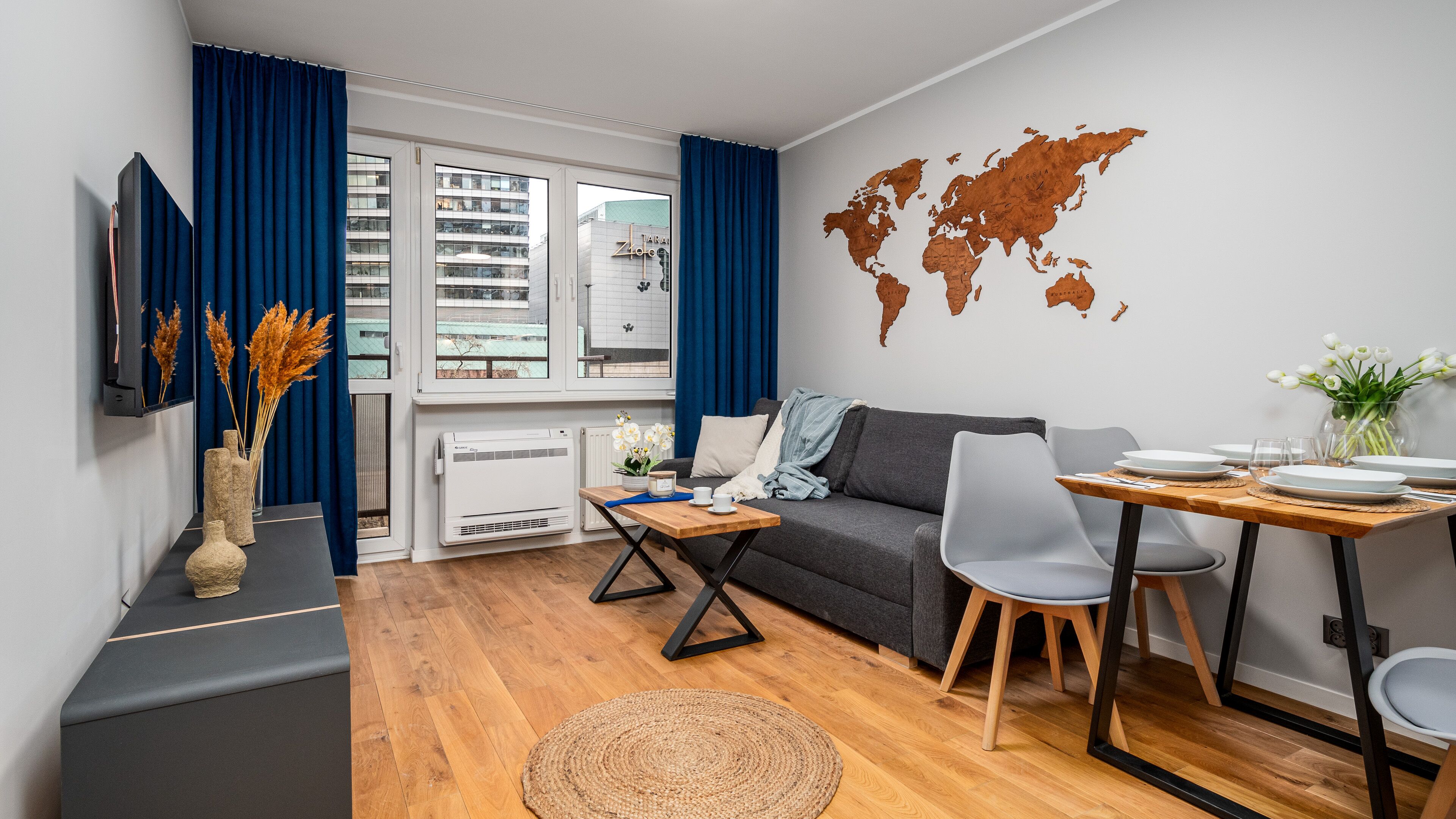 Un salon moderne avec un canapé gris, une table à manger en bois et une carte du monde accrochée au mur.