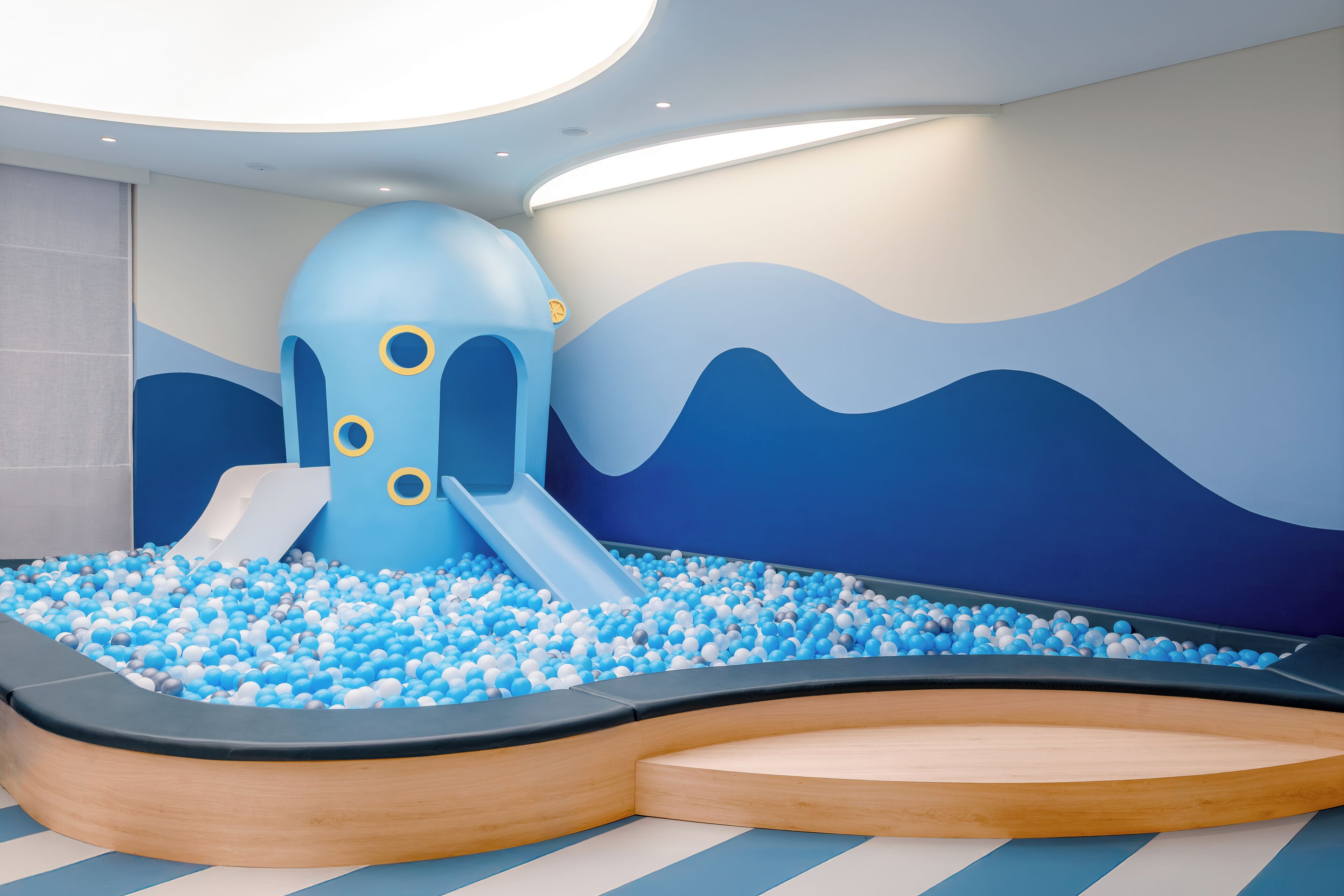 Un área de juegos infantiles con piscina de pelotas, tobogán y una gran estructura azul.
