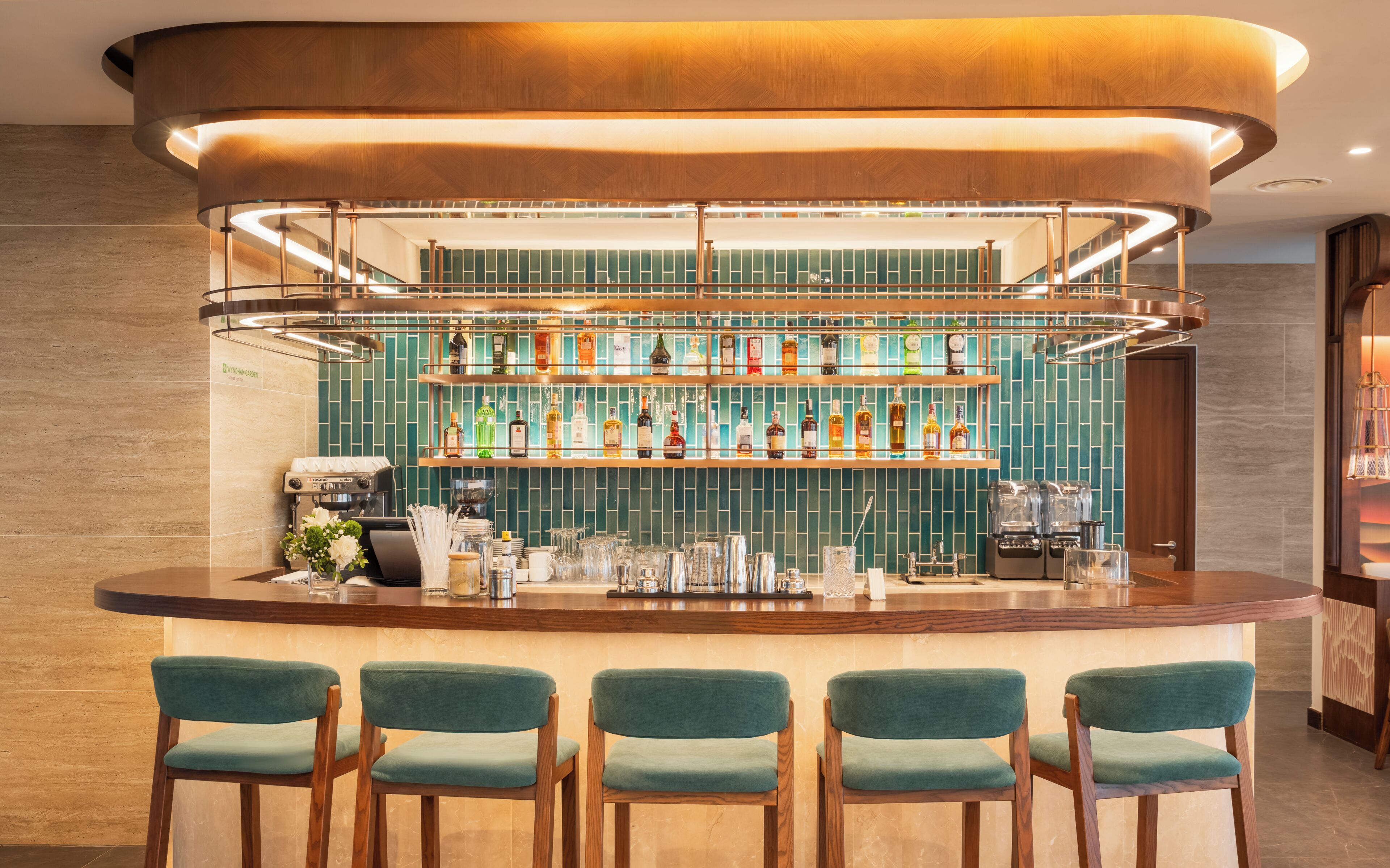 A bar area with a counter, multiple shelves of bottles, and four green upholstered chairs.