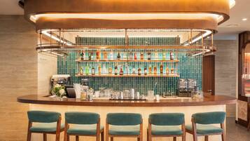 A bar area with a counter, multiple shelves of bottles, and four green upholstered chairs.