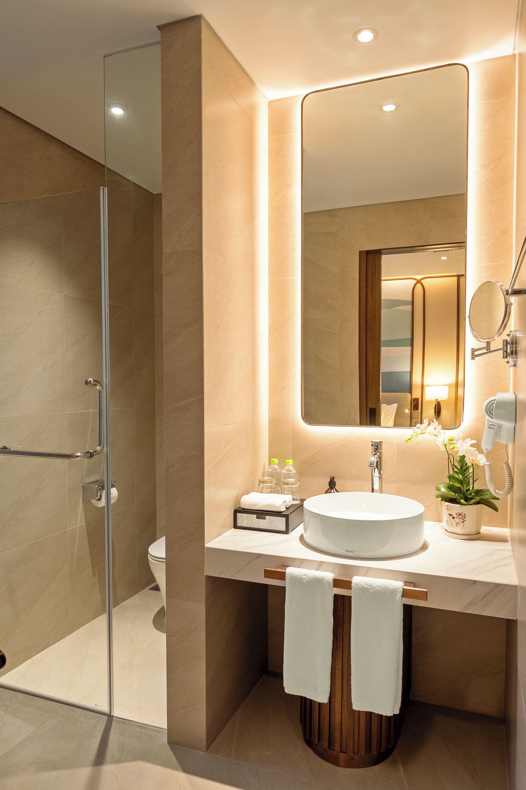 Un bagno moderno con box doccia in vetro, uno specchio grande, un lavabo con mobile contenitore e una pianta in vaso.