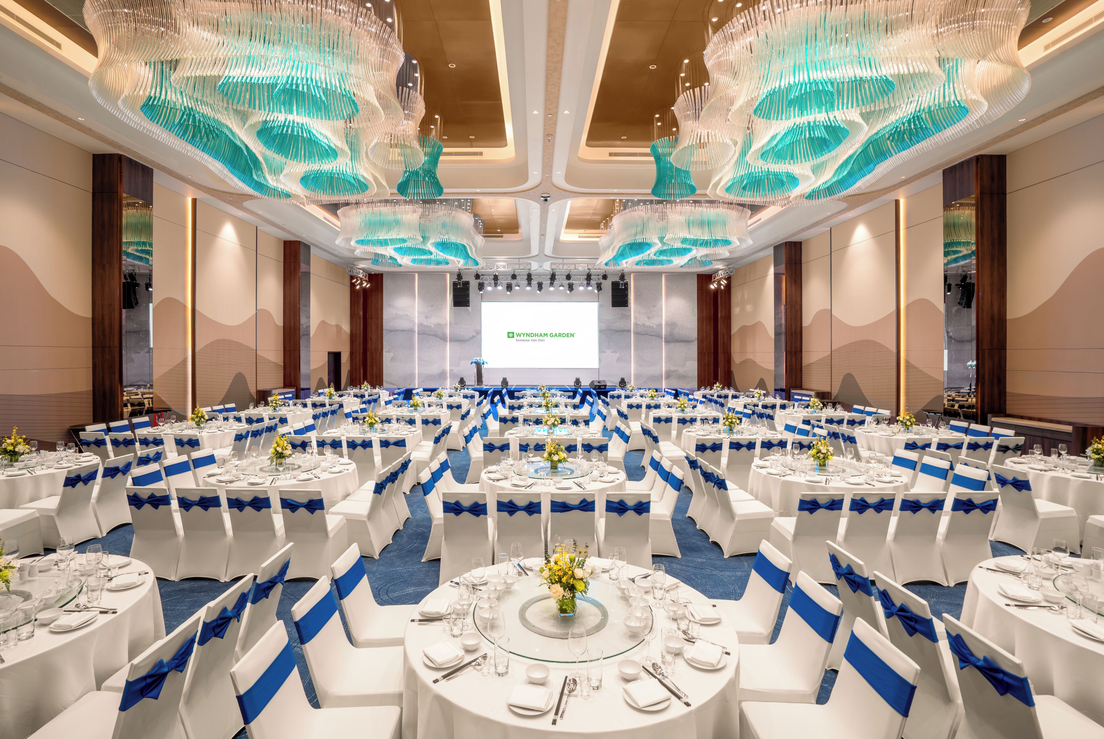 A banquet hall with round tables, blue sashes, and a large screen at the front.