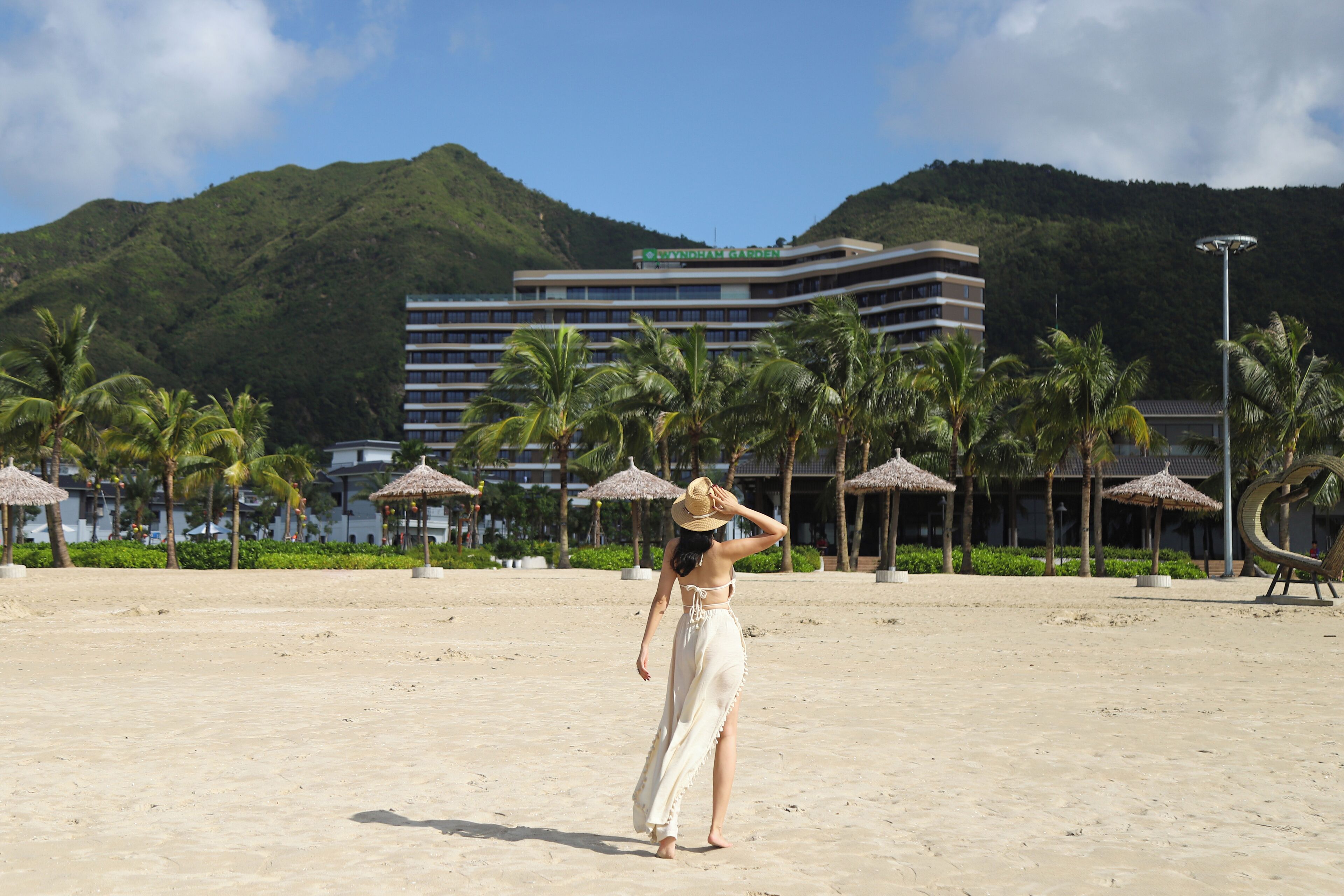 A beach with a hotel in the background, palm trees, and a clear sky.