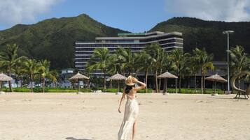 A beach with a hotel in the background, palm trees, and a clear sky.