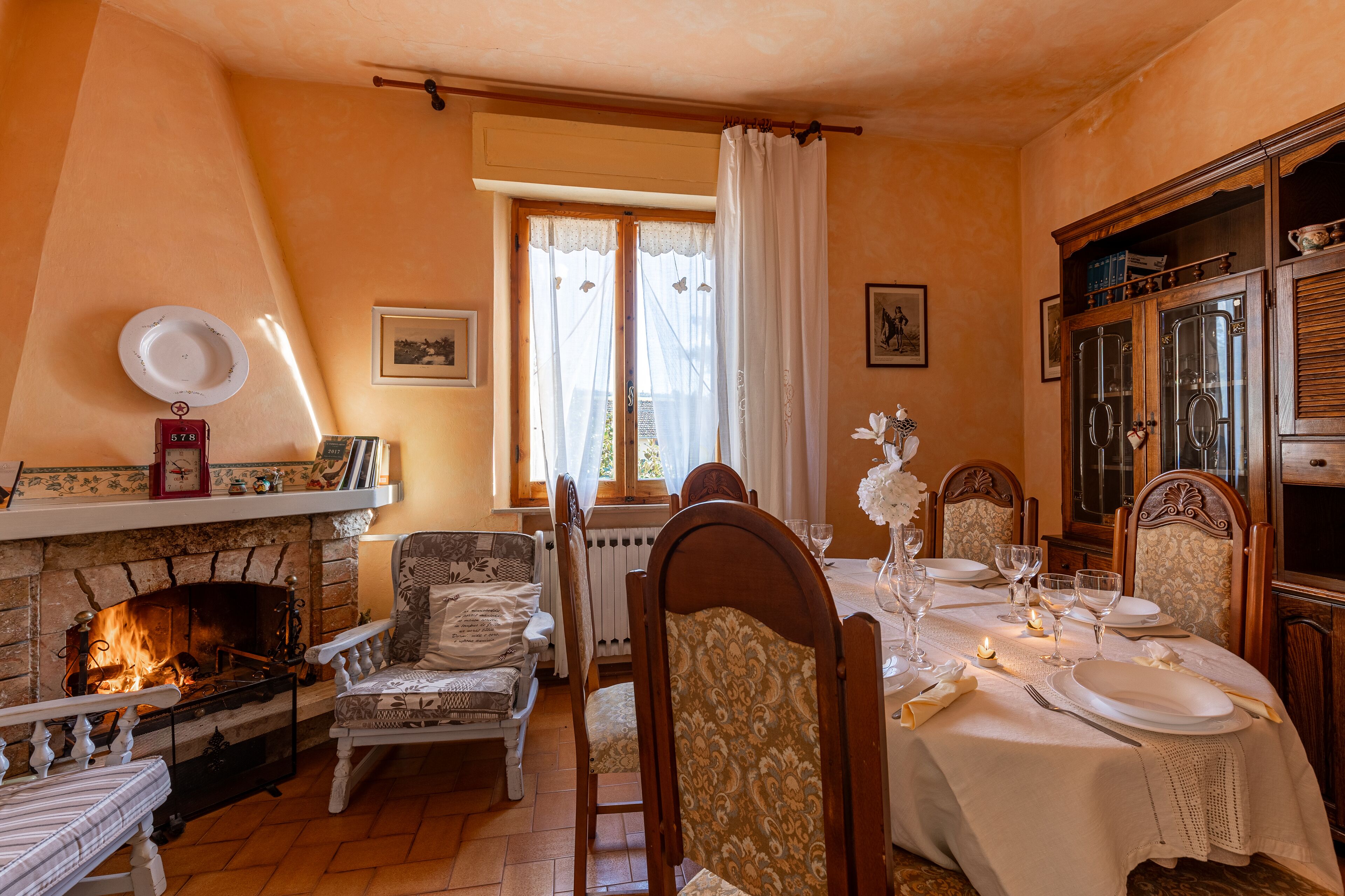A dining room with a fireplace, dining table set for four, and a wooden cabinet with glass doors.