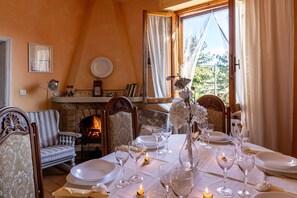 A dining room with a fireplace, a table set for a meal, and a view of the outdoors.