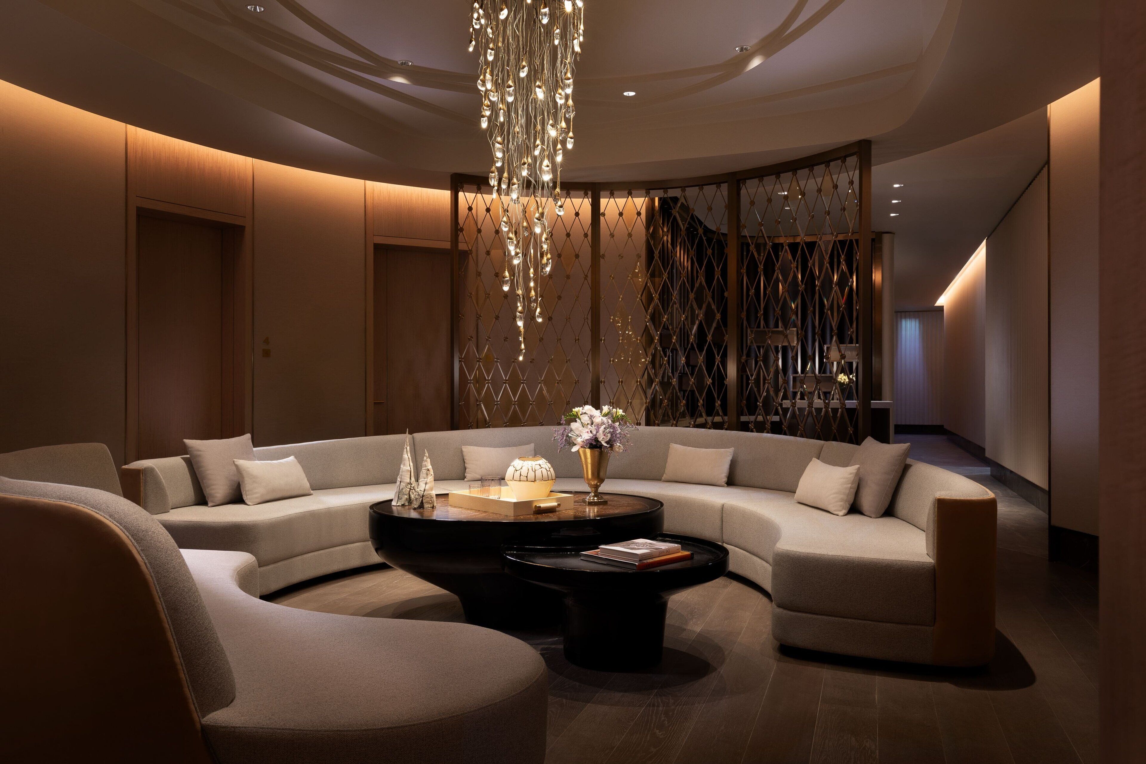 A modern, well-lit living area with a large L-shaped sofa, two black coffee tables, and a decorative chandelier.