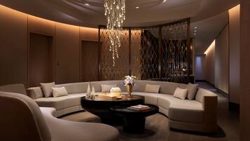 A modern, well-lit living area with a large L-shaped sofa, two black coffee tables, and a decorative chandelier.