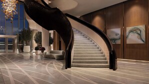 A modern hotel lobby with a curved staircase, a chandelier, and a large window. - The St. Regis Belgrade (Belgrade)