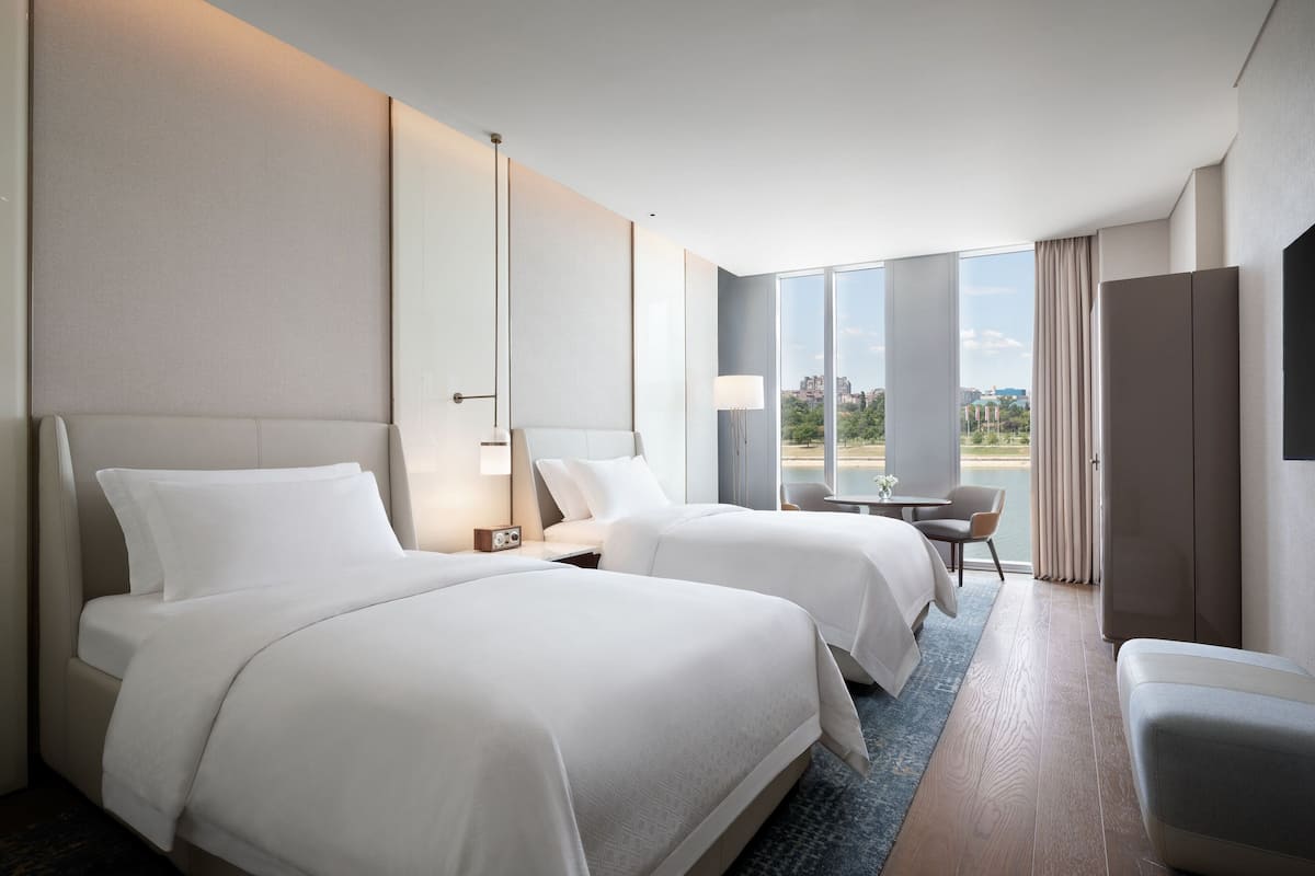 A hotel room with two beds, a desk, and a chair.