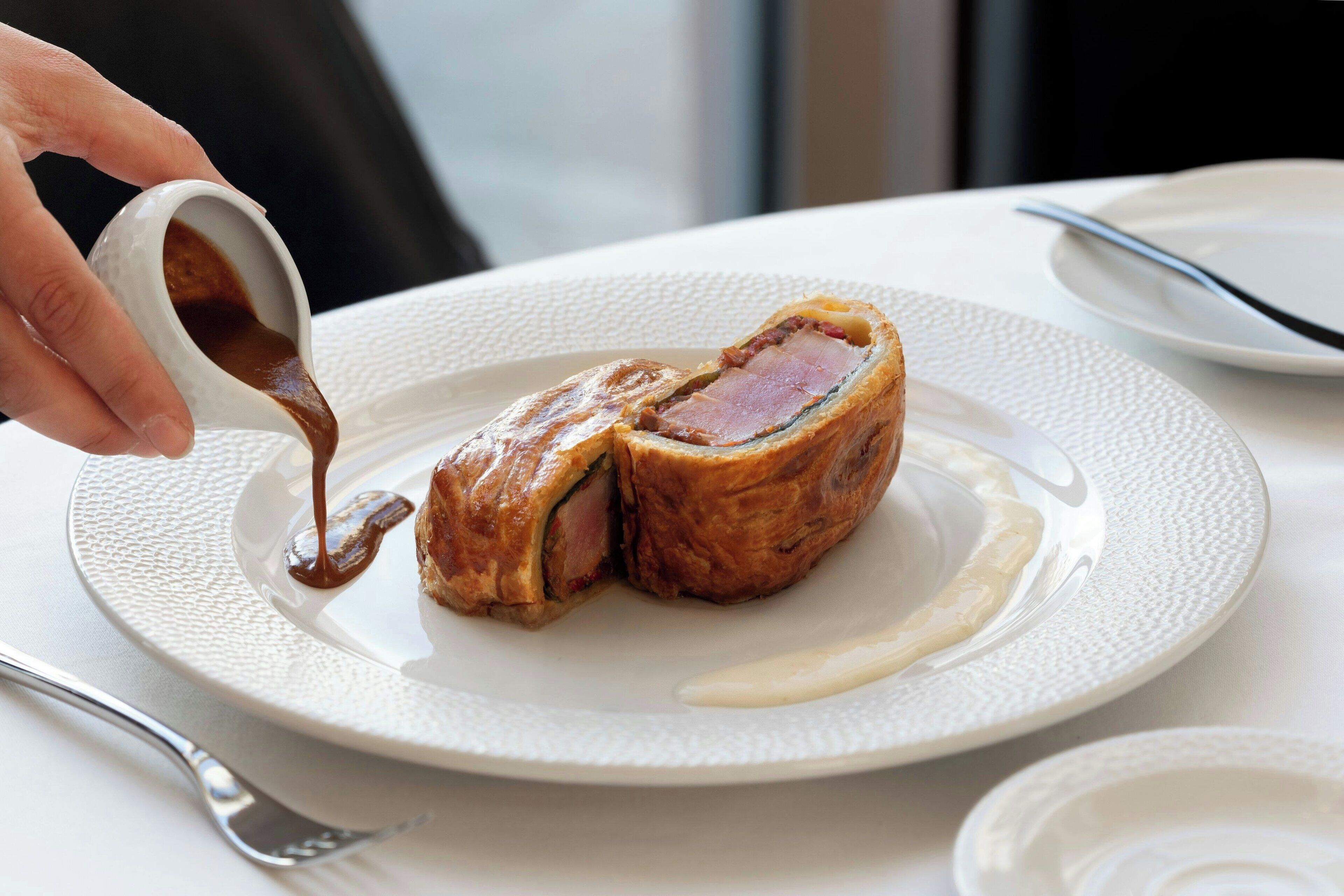 A plate with a pastry and sauce, a fork, and a napkin on a table.