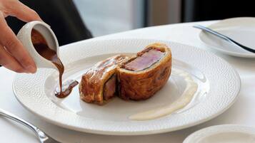 A plate with a pastry and sauce, a fork, and a napkin on a table.