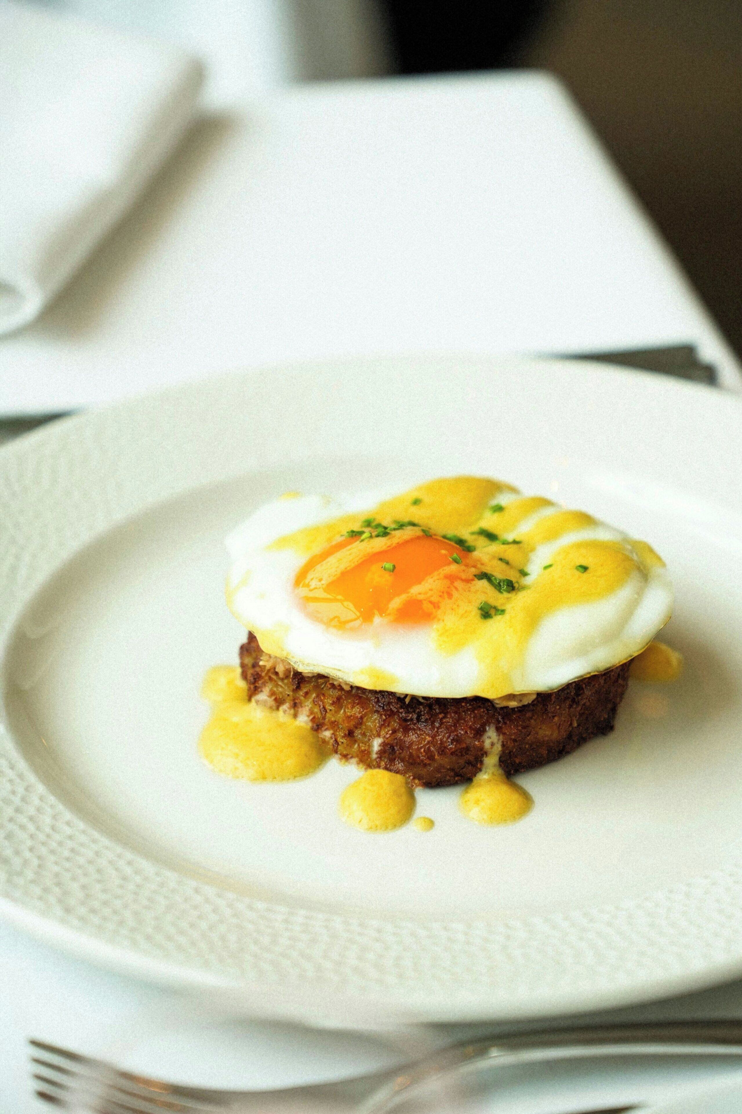 A plate with a dish that includes a poached egg, a slice of meat, and a garnish.