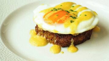 A plate with a dish that includes a poached egg, a slice of meat, and a garnish.