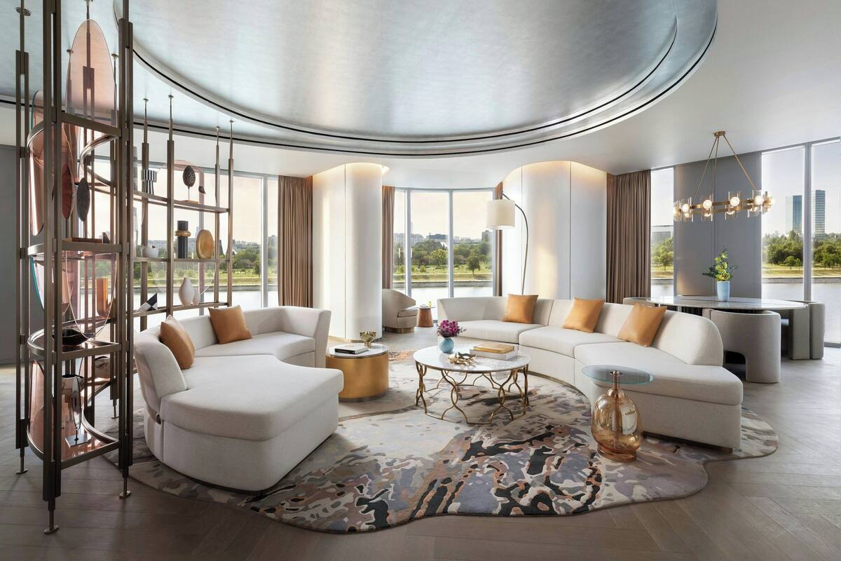 A modern living room with a curved ceiling, white sofas, a coffee table, and a large window offering a city view.