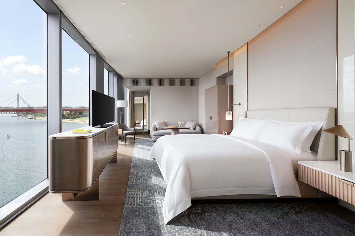 A modern hotel room with a large bed, a desk, and a view of a bridge over water.
