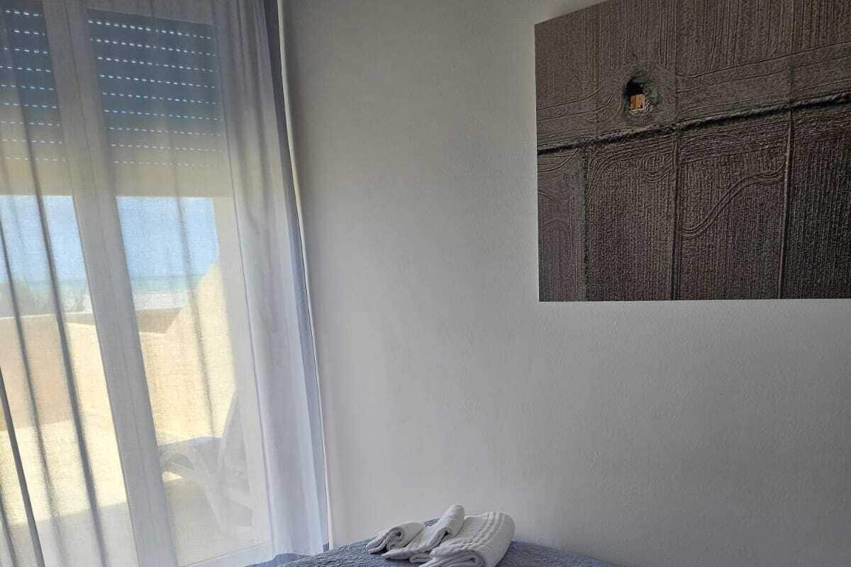 Habitación de hotel con cama, mesita de noche con lámpara y teléfono, ventana con cortinas y una obra de arte colgada en la pared.