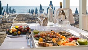 A table set for a meal with seafood and a bottle of champagne, overlooking a beach with umbrellas. - Hotel Stella Marina (Cecina)