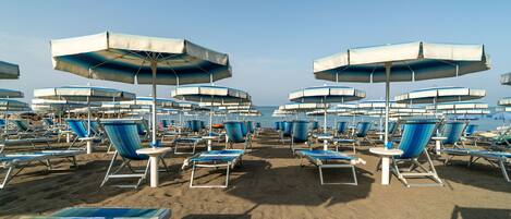 A beach with rows of blue and white sun loungers and umbrellas, arranged in a linear pattern.