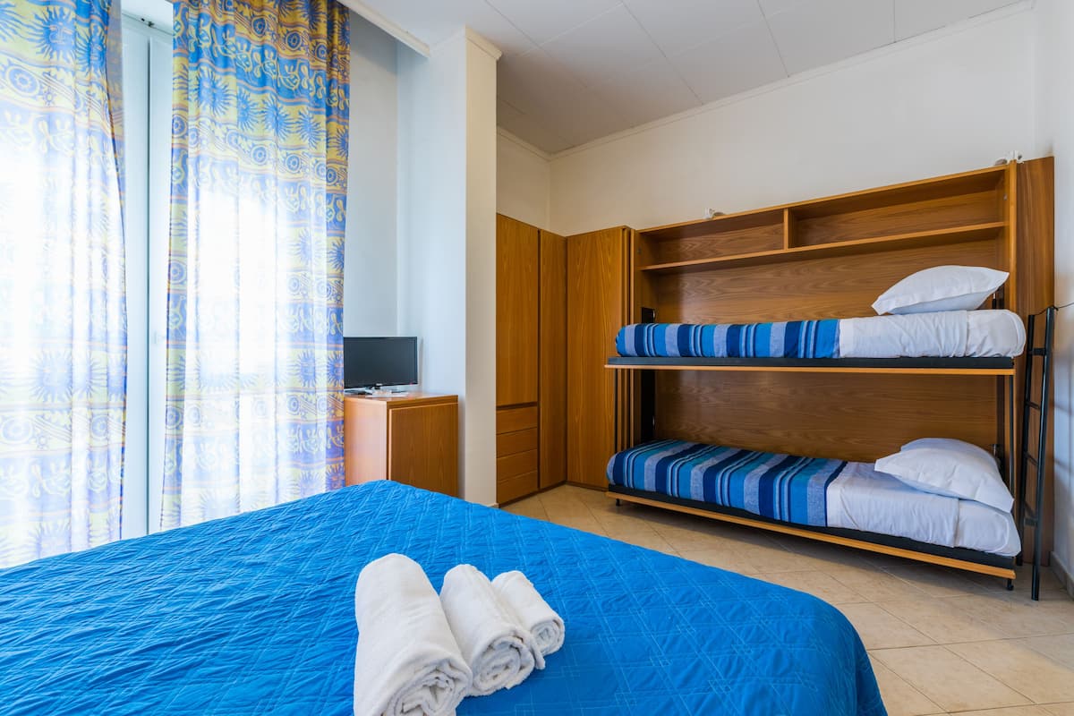 Una habitación con literas, un escritorio con computadora y una ventana con cortinas.
