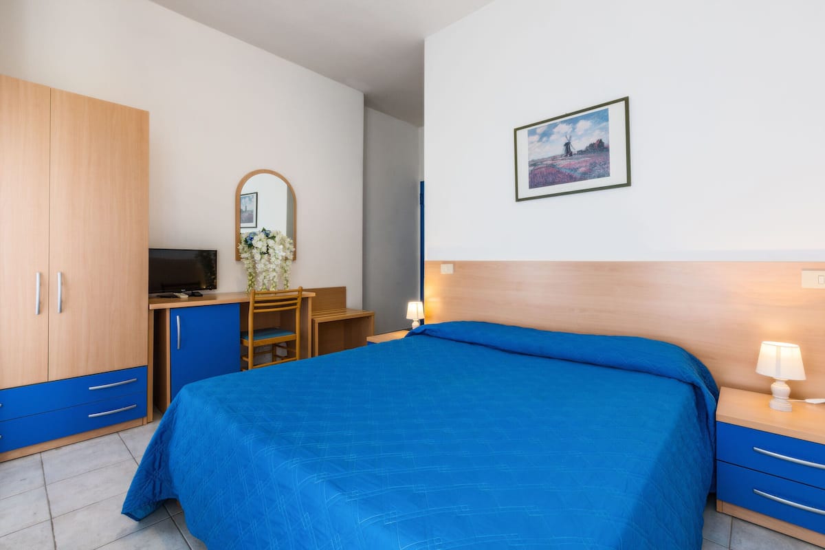 Una habitación de hotel con una cama grande, un escritorio con silla, un televisor y un espejo.