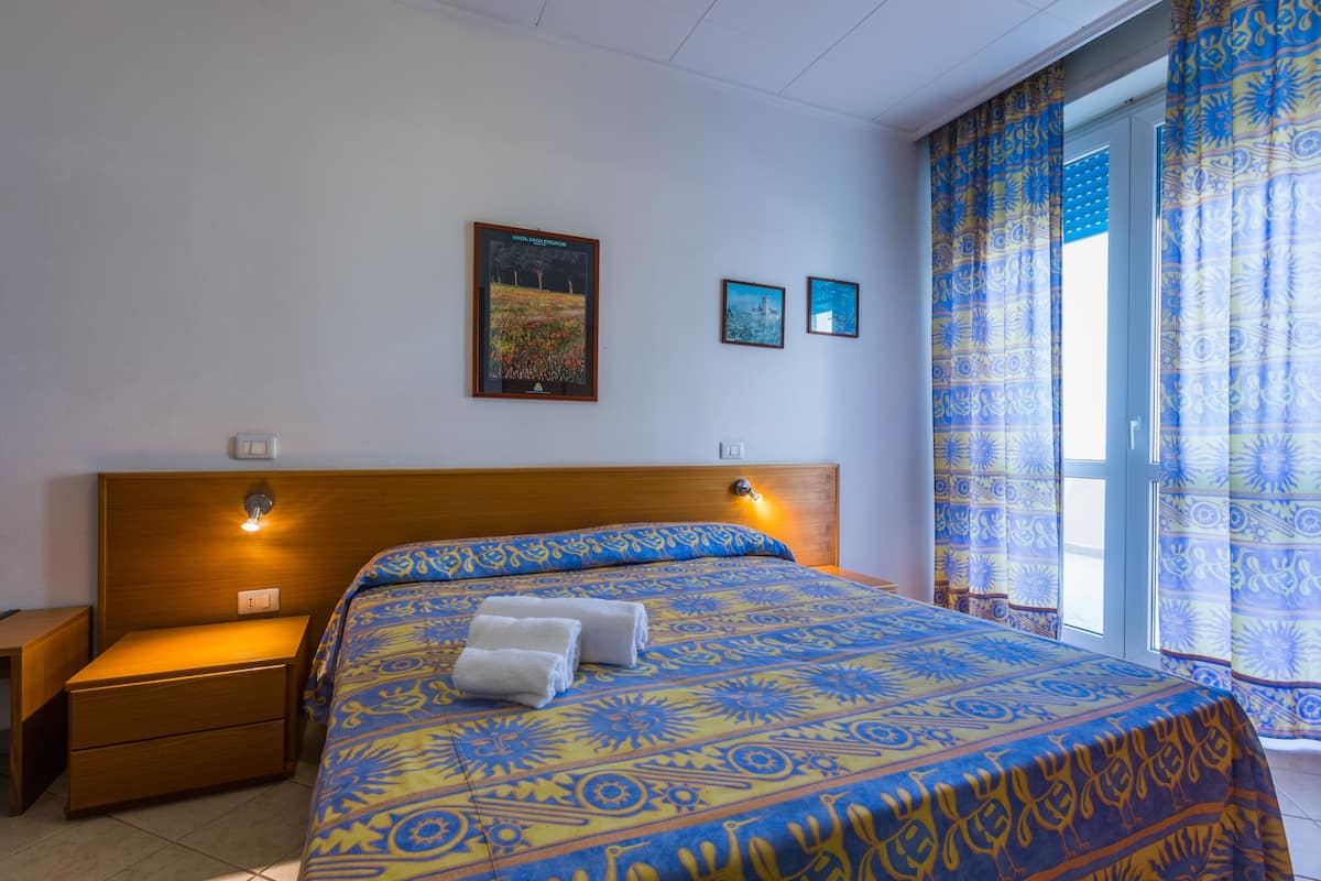Una habitación de hotel con una cama grande, dos mesitas de noche y una ventana con cortinas.