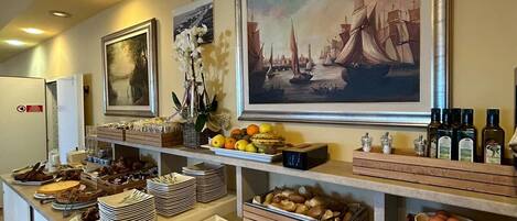 A buffet setup with various food items and a painting of a sailing ship on the wall.