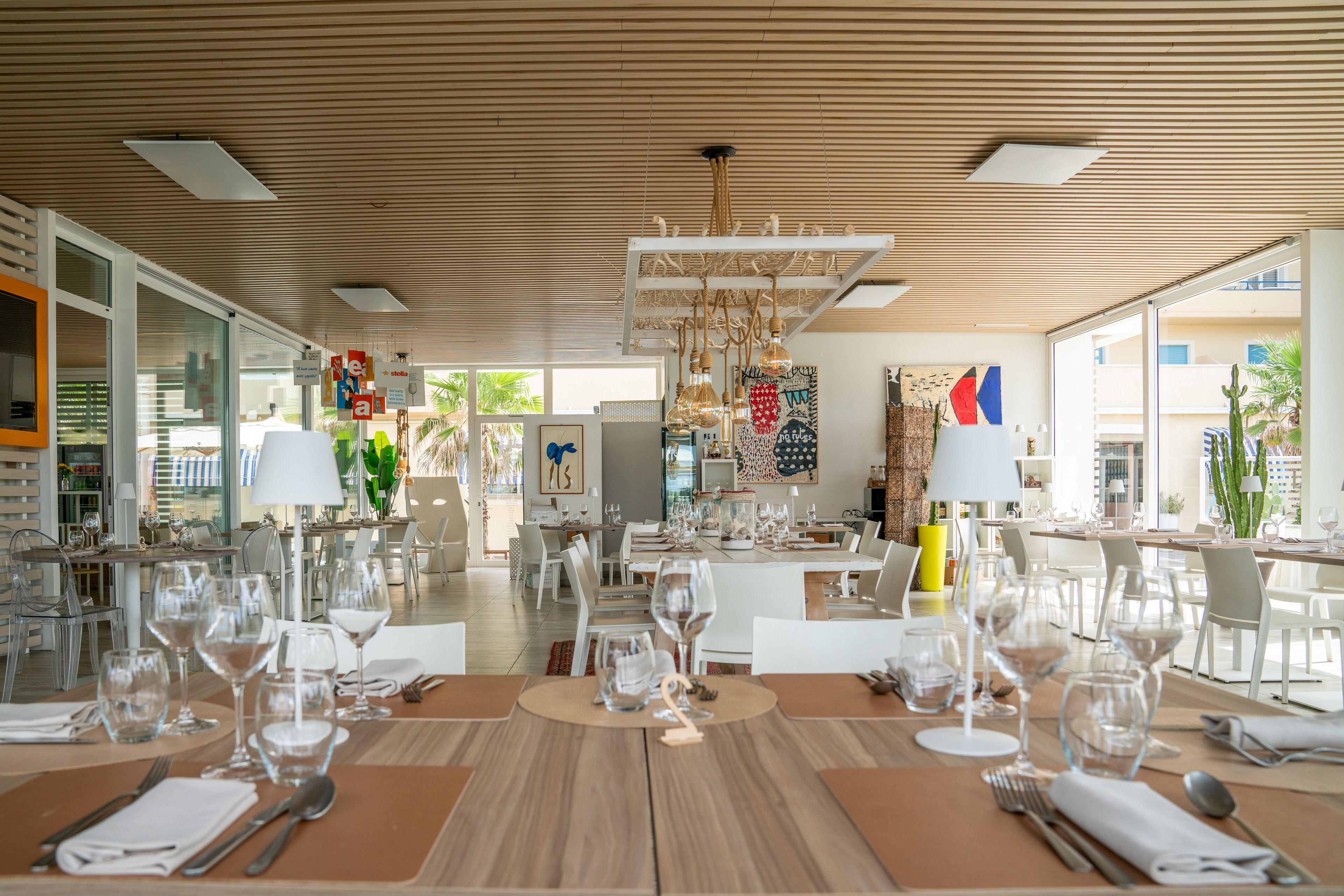 Un comedor moderno con mesas de madera, copas de vidrio transparente y decoración contemporánea.
