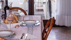 A dining table set with plates, cutlery, a wine glass, and a bottle of wine, with a view of outdoor chairs and a table through a glass door. - Seaside Serenity Flat With Outdoor Pool (Rosolina)